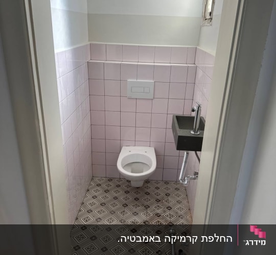 חדר שירותים משופץ עם אסלה תלויה, חיפוי קרמיקה ורוד וריצוף מצויר